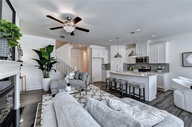 living area with stairway, dark wood-style flooring, a glass covered fireplace, and baseboards