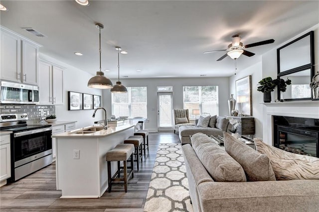 kitchen with a sink, a kitchen breakfast bar, open floor plan, appliances with stainless steel finishes, and tasteful backsplash