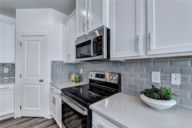 kitchen with light wood-style flooring, appliances with stainless steel finishes, light countertops, white cabinetry, and backsplash