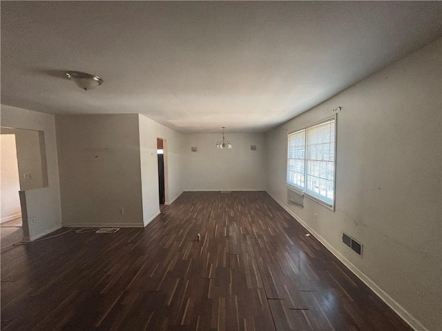 spare room with an inviting chandelier and dark hardwood / wood-style floors