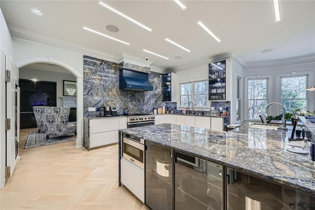 kitchen featuring high end stainless steel range, light parquet flooring, dark stone counters, and extractor fan