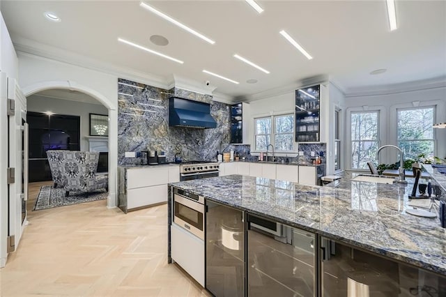 kitchen featuring white cabinets, a fireplace, backsplash, and wall chimney exhaust hood