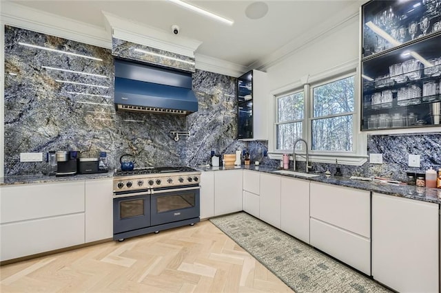 kitchen featuring range with two ovens, crown molding, white cabinetry, a sink, and ventilation hood