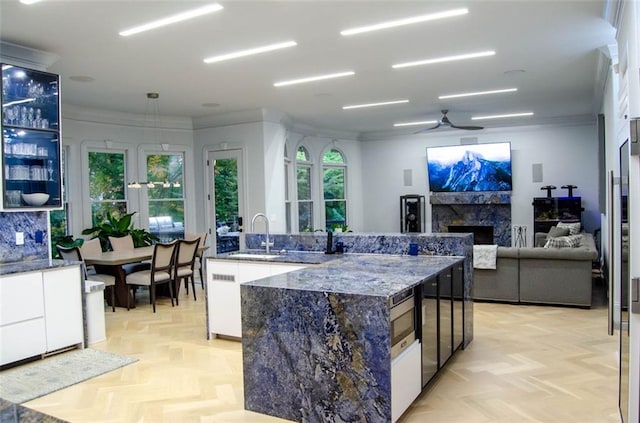 kitchen featuring dark stone countertops, a fireplace, a sink, and white cabinets