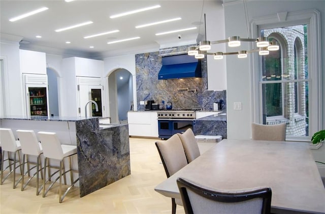 kitchen featuring arched walkways, high quality appliances, white cabinets, a kitchen breakfast bar, and backsplash