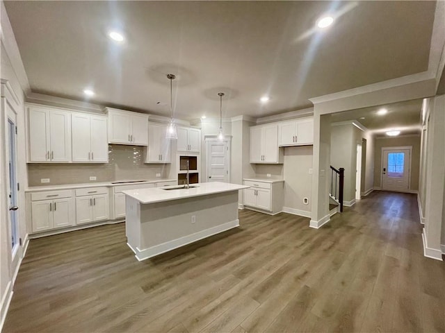 kitchen featuring a kitchen island with sink, white cabinets, sink, hanging light fixtures, and tasteful backsplash