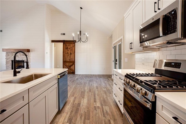 kitchen featuring sink, white cabinets, hanging light fixtures, stainless steel appliances, and a barn door