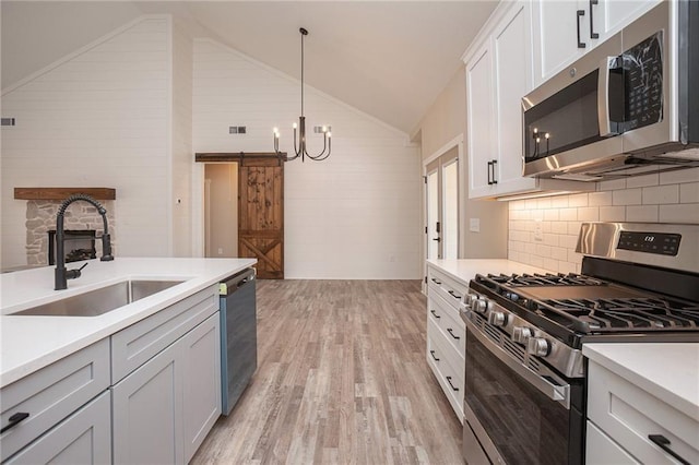 kitchen featuring appliances with stainless steel finishes, white cabinetry, sink, hanging light fixtures, and a barn door