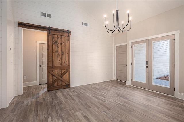 unfurnished dining area featuring a barn door, an inviting chandelier, dark hardwood / wood-style flooring, and french doors