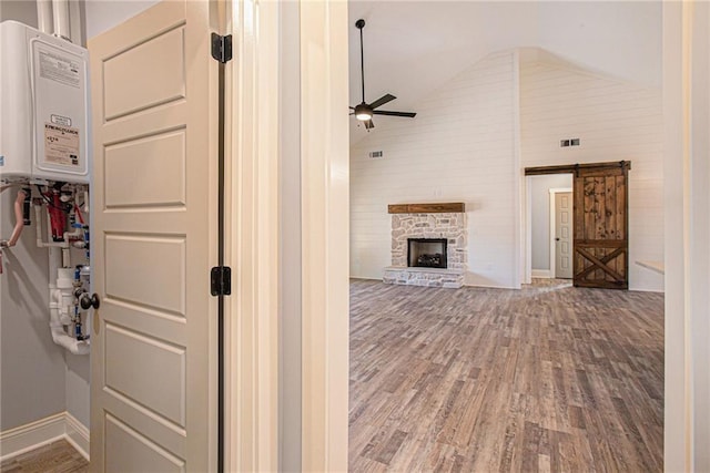 hallway featuring water heater, a barn door, hardwood / wood-style floors, and high vaulted ceiling