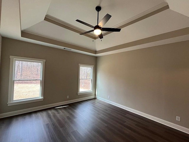 empty room with dark hardwood / wood-style flooring, a tray ceiling, and ceiling fan