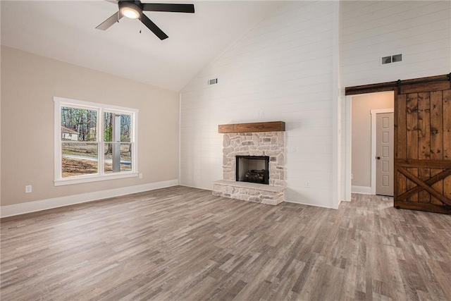 unfurnished living room with wood-type flooring, a barn door, a stone fireplace, and ceiling fan