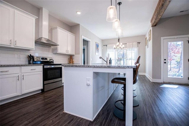 kitchen with a kitchen island with sink, stainless steel electric stove, a kitchen breakfast bar, hanging light fixtures, and white cabinetry