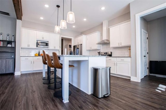 kitchen featuring white cabinets, appliances with stainless steel finishes, a center island with sink, and wall chimney exhaust hood