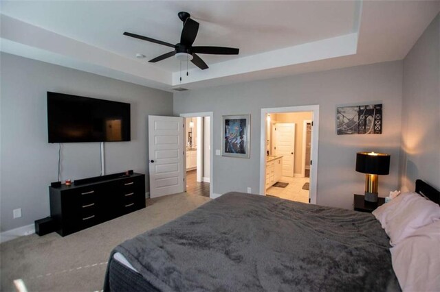 carpeted bedroom featuring a raised ceiling, ceiling fan, and ensuite bathroom