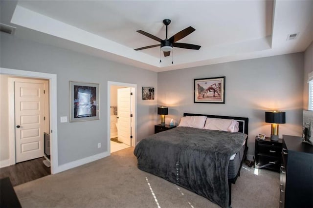 bedroom featuring a raised ceiling, connected bathroom, ceiling fan, and carpet