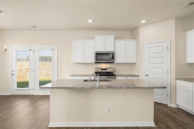 kitchen featuring stainless steel appliances, a center island with sink, white cabinets, and light stone counters