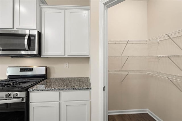 kitchen with dark wood-type flooring, appliances with stainless steel finishes, dark stone counters, and white cabinets