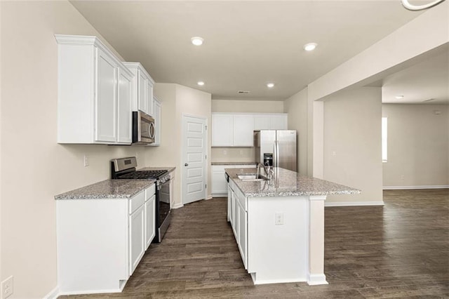 kitchen with sink, white cabinets, stainless steel appliances, light stone countertops, and a center island with sink