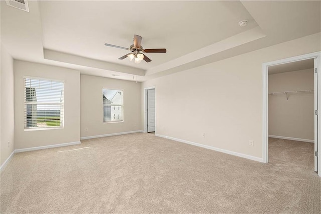 unfurnished bedroom featuring a spacious closet, light colored carpet, a raised ceiling, and ceiling fan