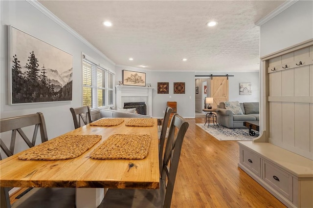 dining area featuring light wood-type flooring, a textured ceiling, crown molding, and a barn door