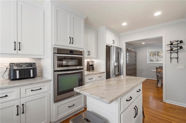 kitchen with white cabinetry, appliances with stainless steel finishes, ornamental molding, light hardwood / wood-style flooring, and light stone counters