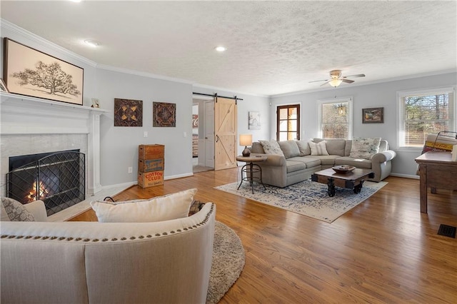 living room with ceiling fan, ornamental molding, a barn door, and wood-type flooring