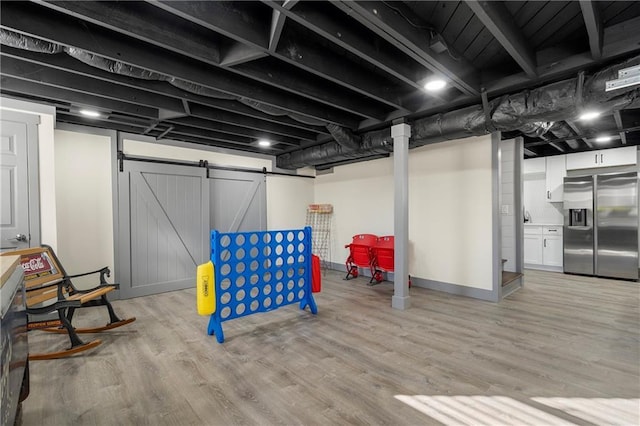 basement featuring stainless steel refrigerator with ice dispenser, light hardwood / wood-style flooring, and a barn door