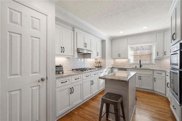 kitchen featuring light stone countertops, appliances with stainless steel finishes, a kitchen island, white cabinetry, and a breakfast bar