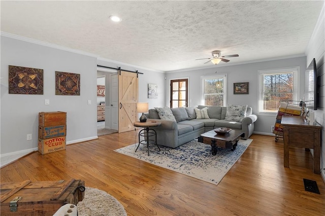 living room featuring ceiling fan, a barn door, crown molding, and hardwood / wood-style floors