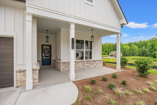 view of exterior entry featuring covered porch, brick siding, and board and batten siding