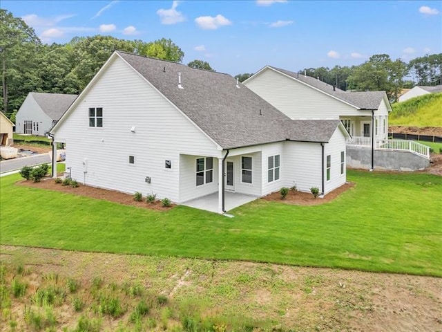 back of house featuring a yard, roof with shingles, and a patio area