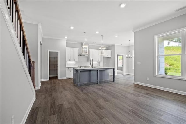 kitchen with baseboards, visible vents, white cabinets, an island with sink, and light countertops