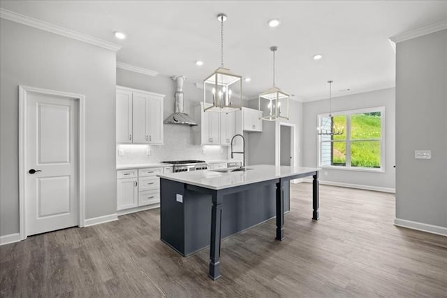 kitchen with wall chimney range hood, white cabinetry, ornamental molding, and a sink