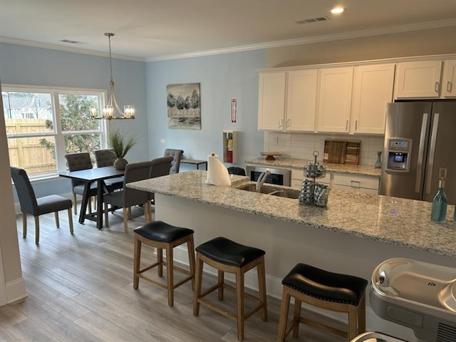 kitchen featuring light wood finished floors, stainless steel fridge, white cabinets, ornamental molding, and backsplash