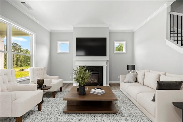 living area featuring a glass covered fireplace, crown molding, stairway, and wood finished floors