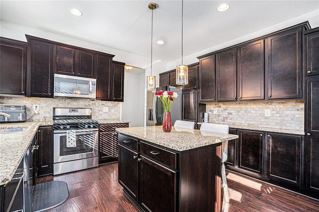 kitchen with light stone countertops, pendant lighting, a kitchen island, and stainless steel appliances