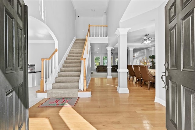 foyer entrance with hardwood / wood-style floors, ceiling fan, ornate columns, and crown molding