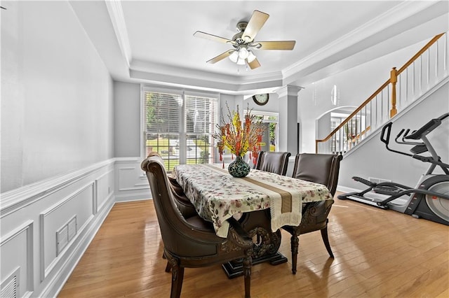 dining space featuring ceiling fan, a raised ceiling, light hardwood / wood-style flooring, decorative columns, and crown molding