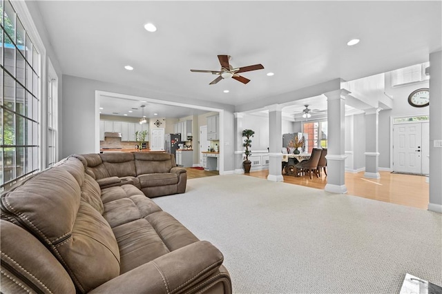 carpeted living room with ceiling fan and ornate columns