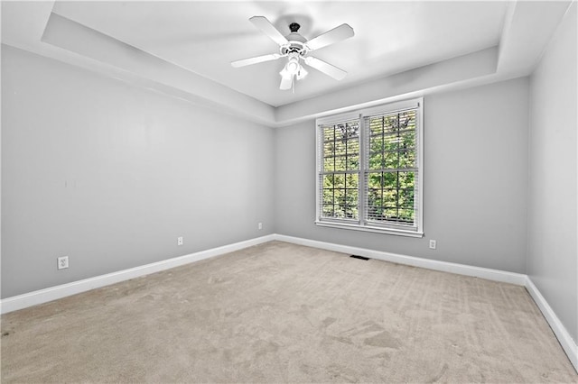 carpeted spare room with a raised ceiling and ceiling fan