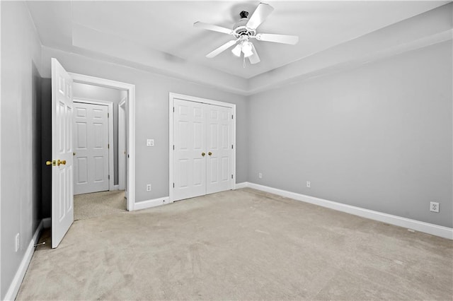 unfurnished bedroom featuring a tray ceiling, ceiling fan, and light colored carpet