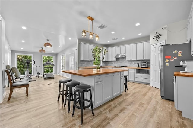 kitchen with pendant lighting, butcher block countertops, stainless steel appliances, and light hardwood / wood-style floors