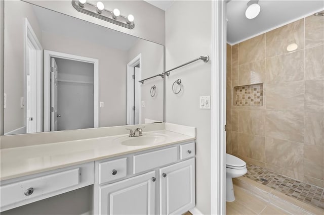 bathroom featuring tile patterned floors, vanity, a tile shower, and toilet