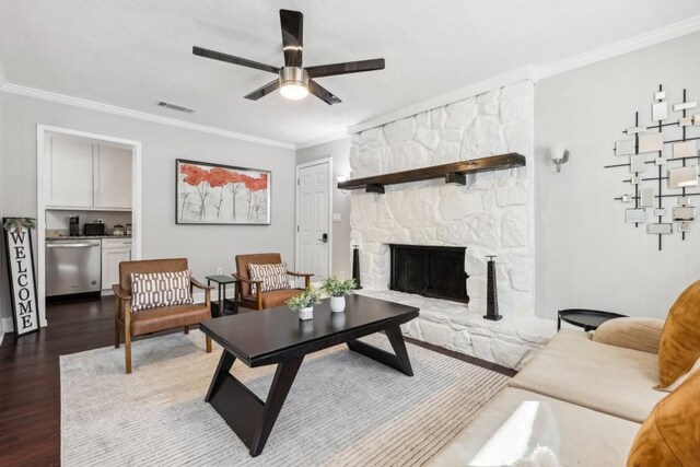 living room with a stone fireplace, crown molding, hardwood / wood-style floors, and ceiling fan