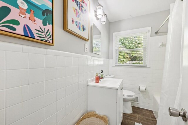 full bathroom featuring wood-type flooring, tile walls, shower / bath combo with shower curtain, toilet, and vanity