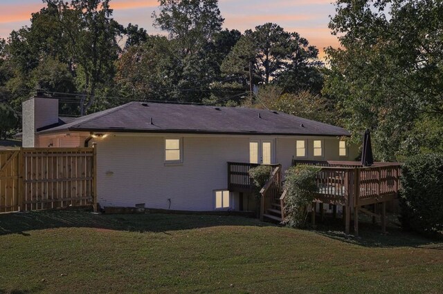 back house at dusk featuring a deck and a lawn