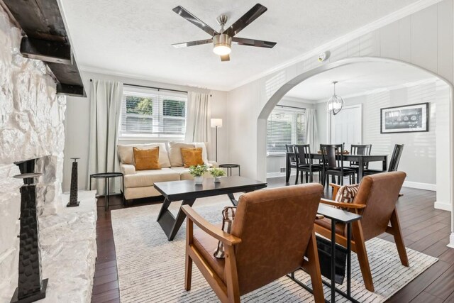 living room featuring crown molding, dark hardwood / wood-style floors, ceiling fan with notable chandelier, and a fireplace