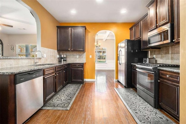 kitchen with appliances with stainless steel finishes, backsplash, dark brown cabinets, light stone counters, and sink