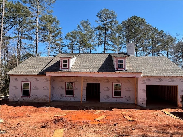 unfinished property with a garage, a chimney, and a shingled roof